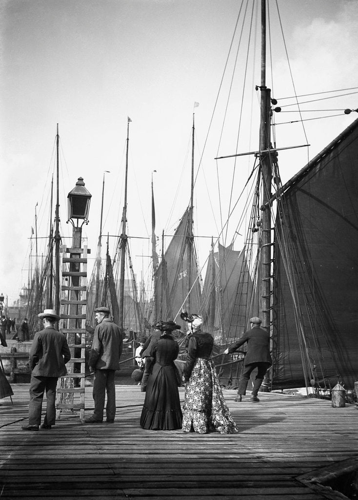 Detail of Men and women onlookers at the end of the quay looking at the forest of masts and sails in the harbour at Lowestoft, Suffolk by Smiths Suitall Ltd.