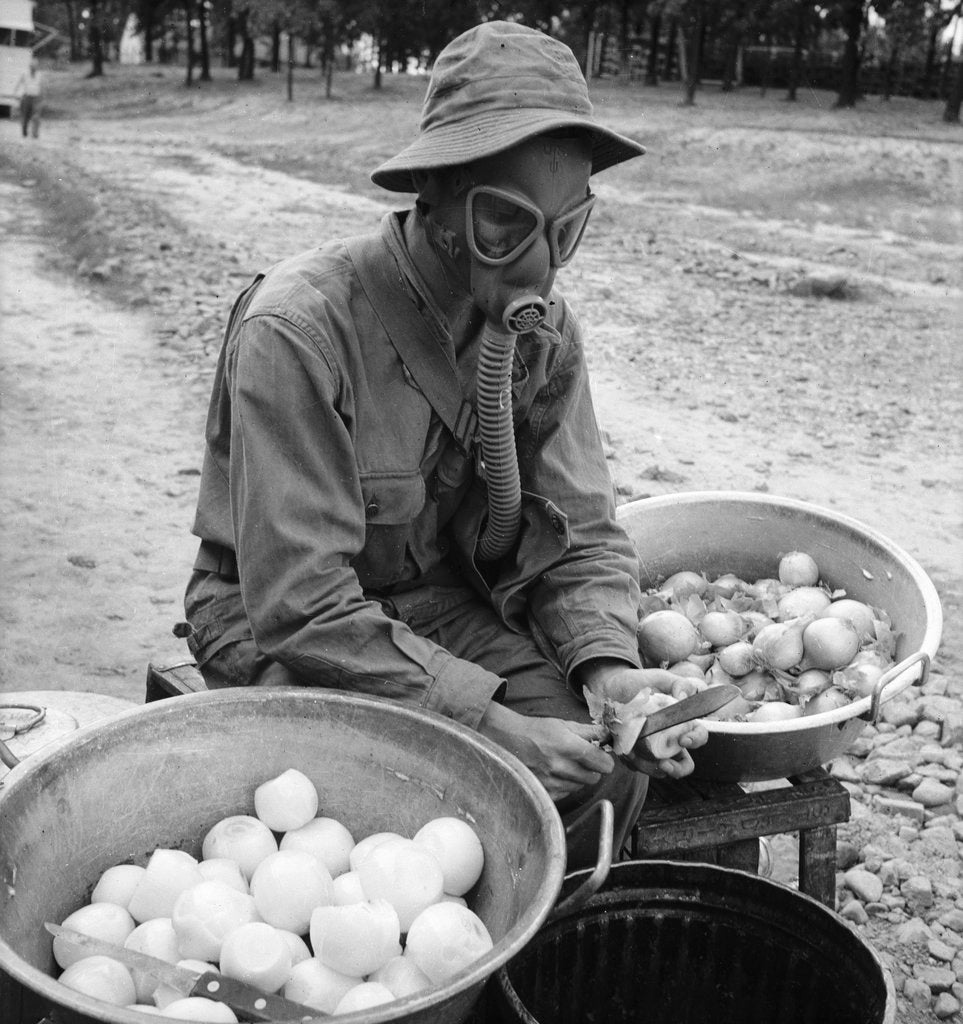 Detail of American soldier peeling onions while wearing a gas mask by Alan Villiers