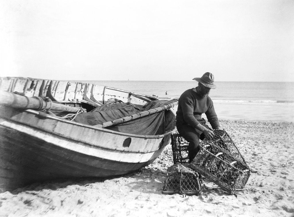 Detail of A fisherman in sou'wester mending lobster/crab creels on the beach alongside a beached Sheringham crab boat by Smiths Suitall Ltd.