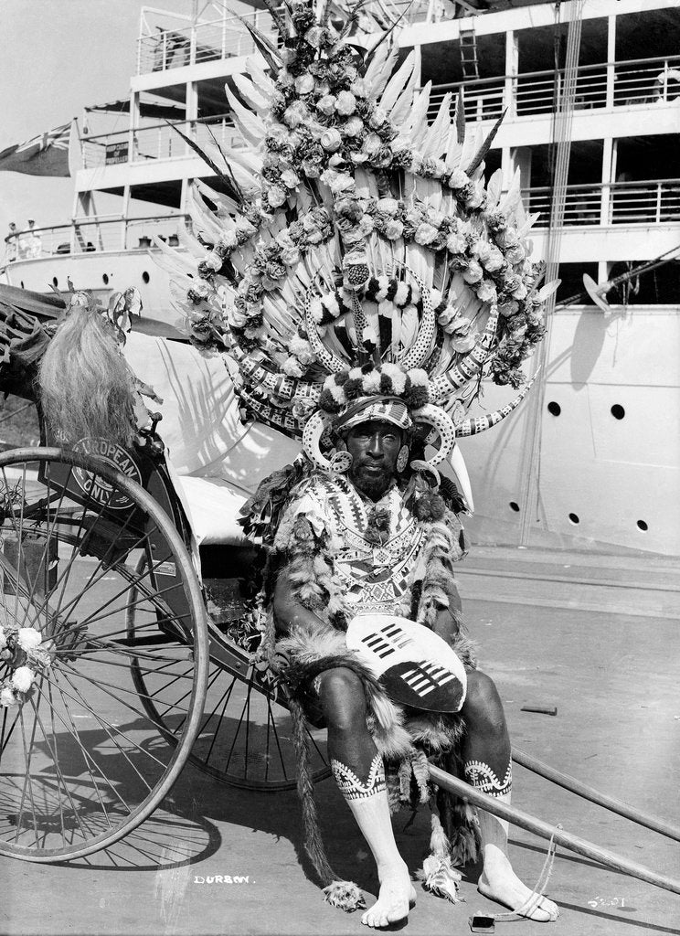 Detail of A local rickshaw driver in 'traditional' costume, with a Union-Castle Line ship in the background, at Durban, South Africa by Marine Photo Service